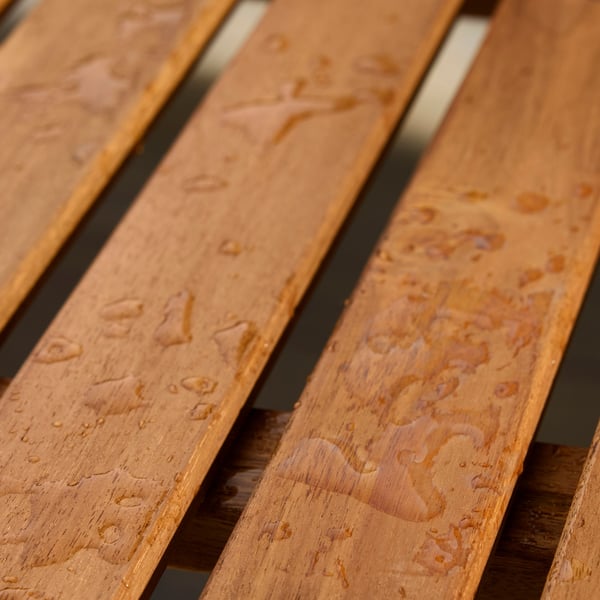 A close-up of a wooden table where raindrops are forming beads on the surface.