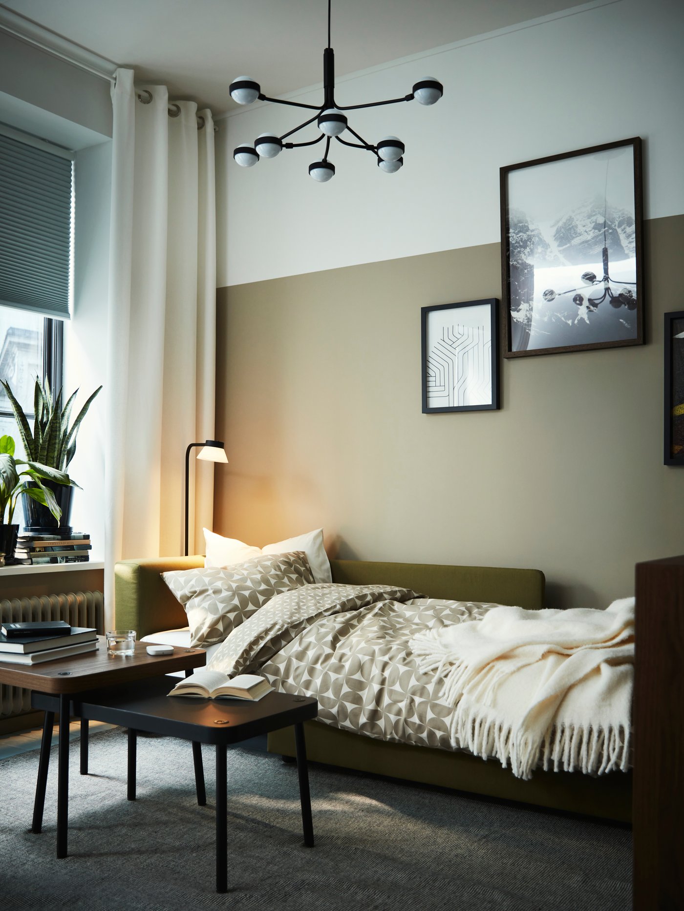 Un living con un sofá cama de un cuerpo SKÖNABÄC que tiene mantas y almohadas puestas para ser usado.