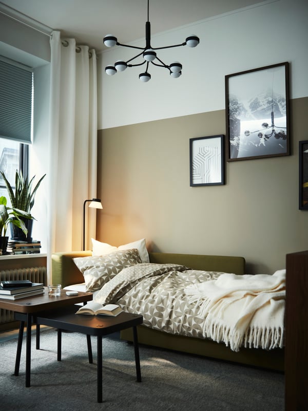 A black/white 8-armed STORSLINGA LED chandelier hangs from a ceiling above a sofa-bed and a SONHULT nest of tables, set of 2.