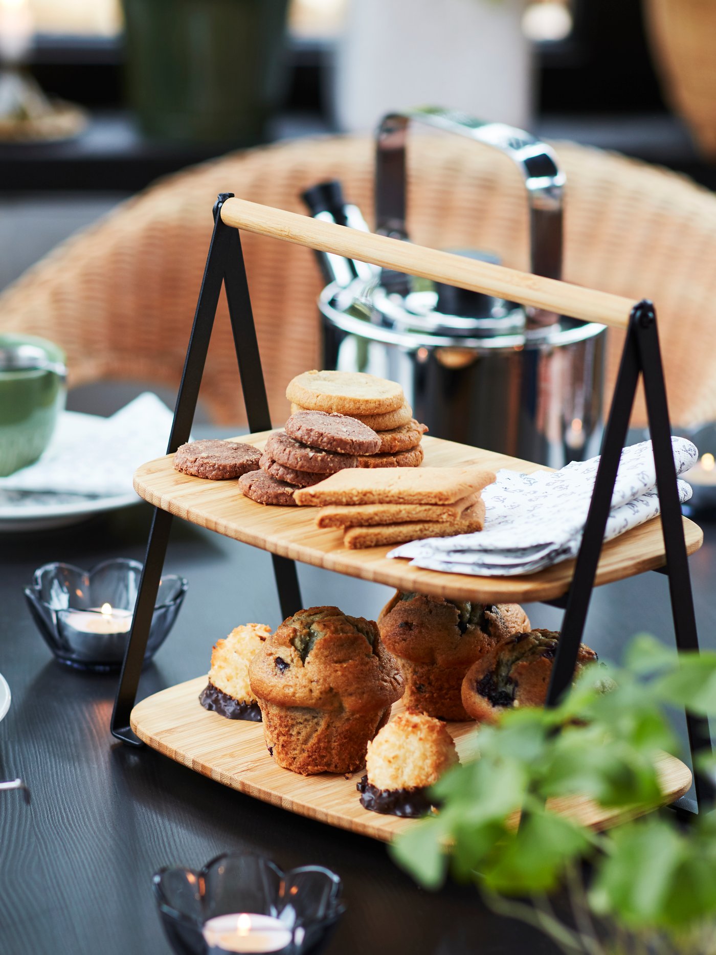 A FULLSPÄCKAD serving tray loaded with various biscuits and muffins as well as some napkins. In the background is a teapot.