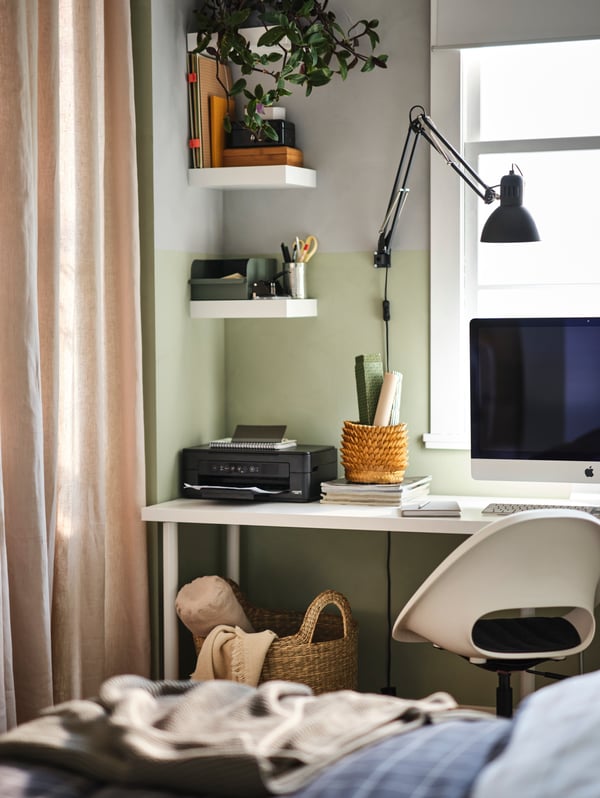 An office space in a bedroom with a LAGKAPTEN/ADILS desk and LOBERGET/MALSKÄR swivel chair with white LACK shelves above.