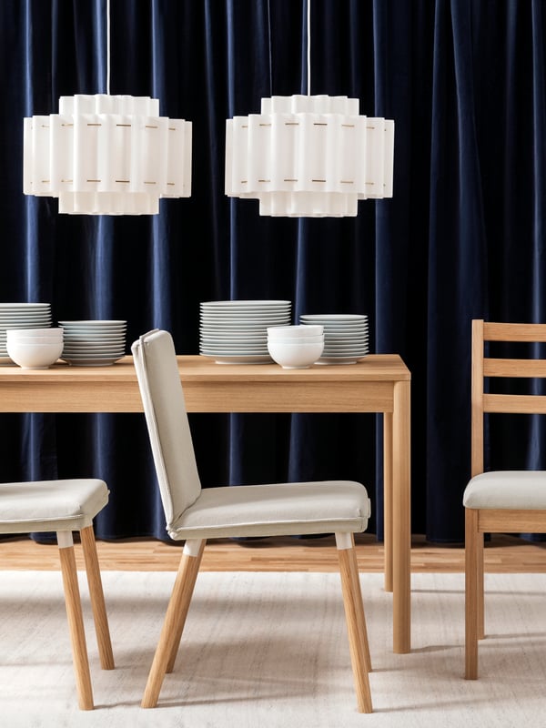 A bright dining space with a light wood TONSTAD chair beside a table set with plates and vases under stylish lamps.