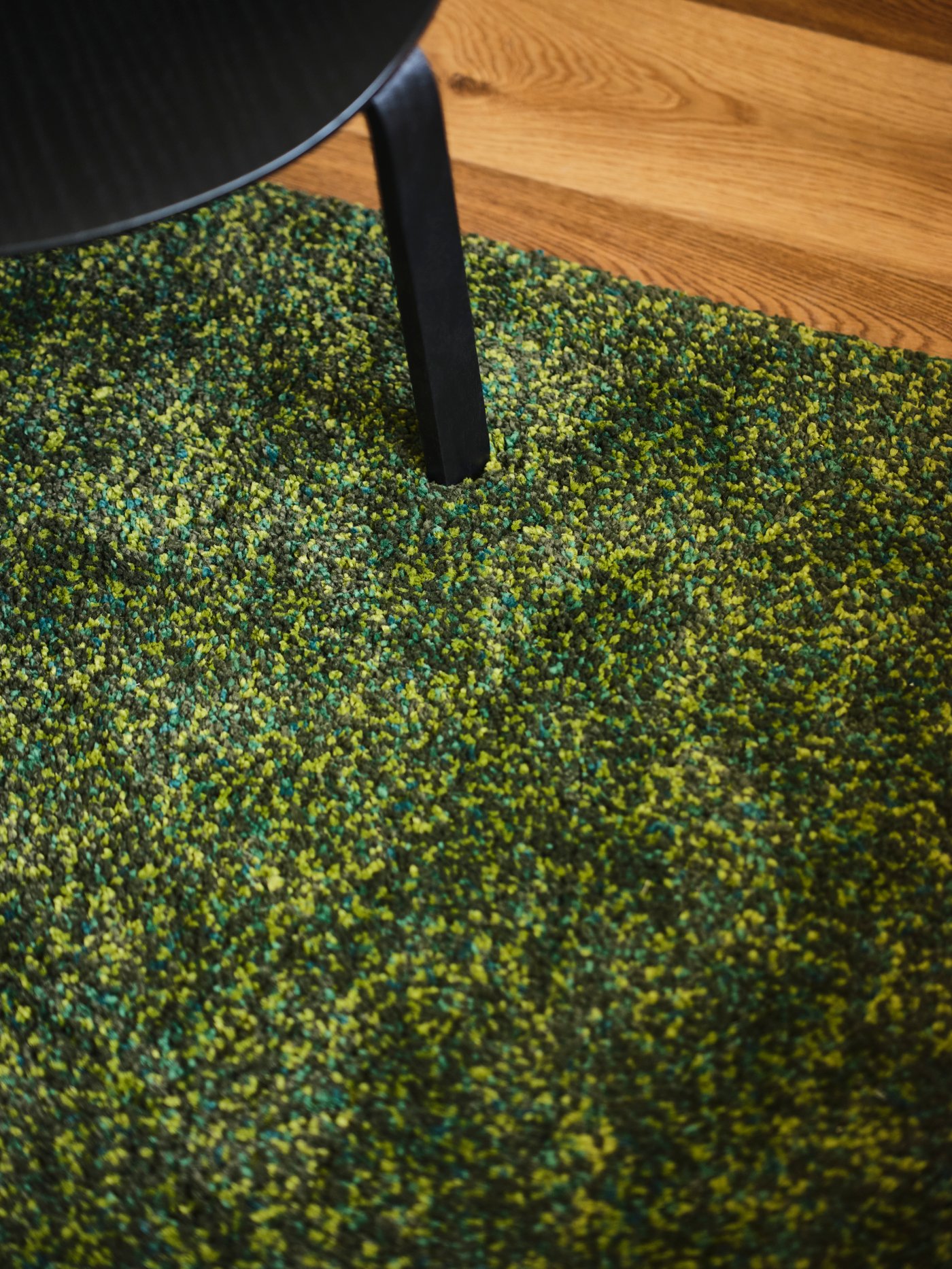 A green, high pile VINDUM rug with a chair on a wooden floor.