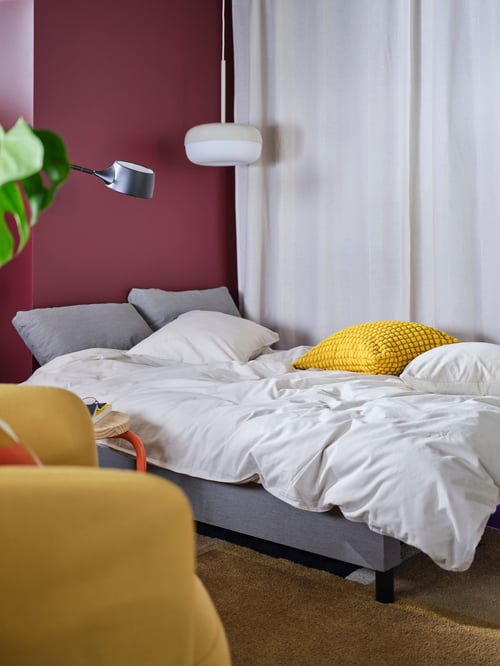 Wohnzimmer mit einem ÄLVDALEN Bettsofa mit der ÄNGSLILJA Bettwäsche. Darüber hängt eine BLÅSVERK Hängeleuchte, neben dem Sofa ist eine VÅGHÖJD Standleuchte zu sehen.
