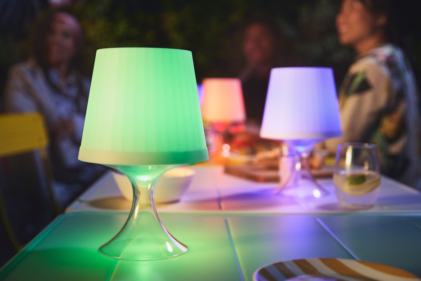 An outdoor seating area is set with LAMPAN lamps in blue, red, and green, lighting up an evening chat.