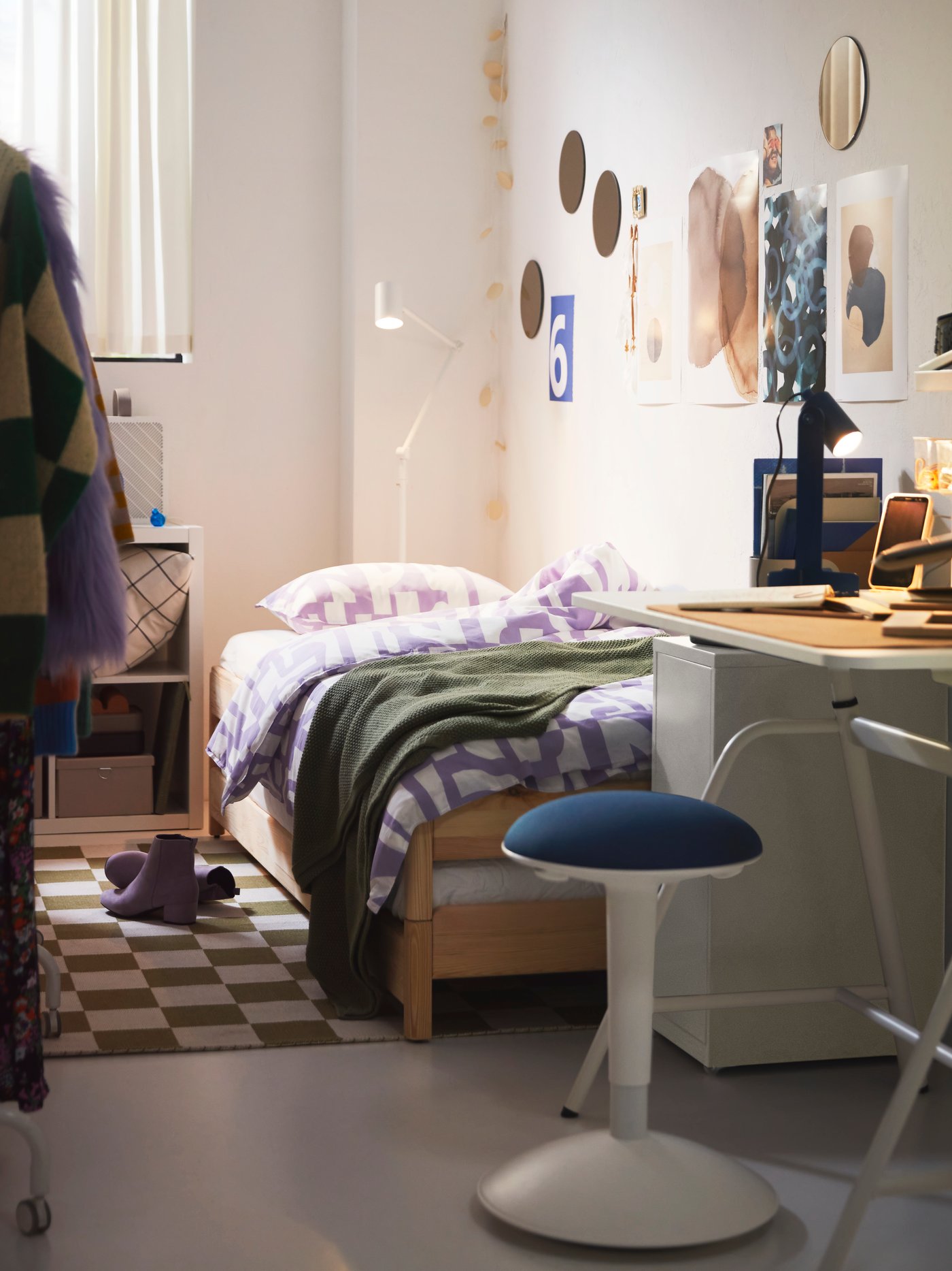 A college dorm with a white and purple bedding on a bed frame next to a small desk with a lamp on it.
