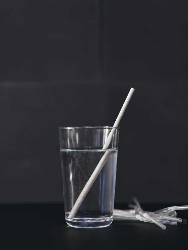 A FÖRNYANDE drinking straw rests in a filled glass, with single-use plastic straws in the background.