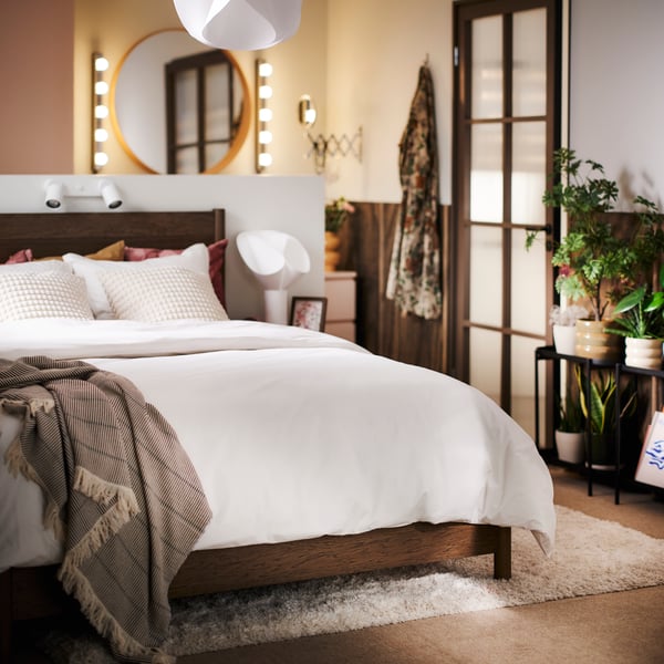 A brown TONSTAD bed with storage, covered with HAMPFLOCKEL bed linen and with a LAPPKATTFOT throw on top.