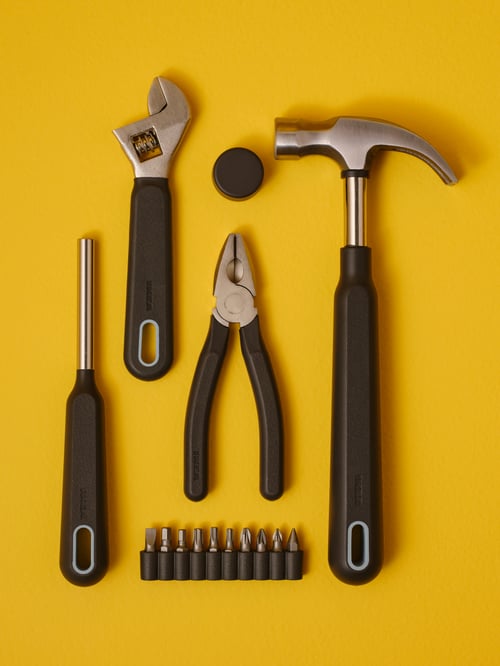 A TRIXIG tool set consisting of a claw hammer, combination pliers, a wrench, and a screwdriver, all set on a yellow surface.