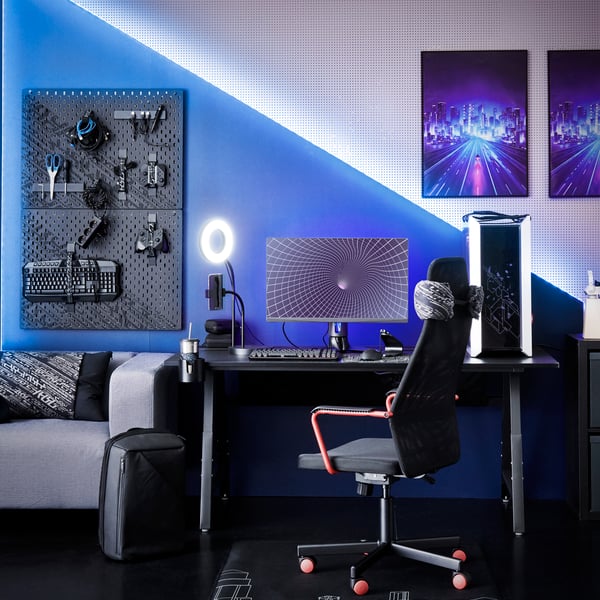 Ett gamingrum med svart golv och vita väggar upplyst i blått och inrett med svart gamingbord och gamingstol.