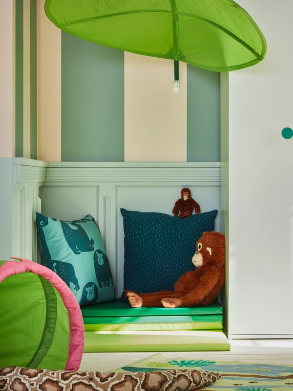 A green, leaf-shaped LÖVA bed canopy shelters a cosy little nook with cushions, soft toys and a PLUFSIG folding gym mat.