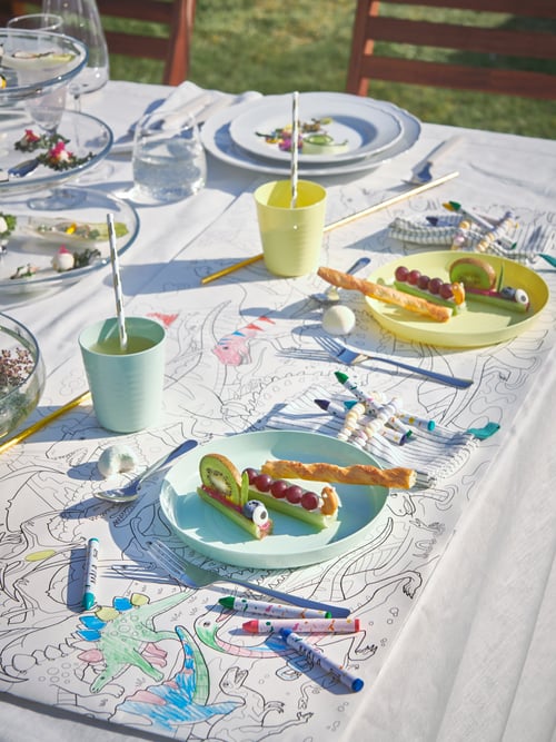Outdoor featuring multiple multicolour wax crayons with paper wrapping, a colouring paper roll and multiple mugs and plates.
