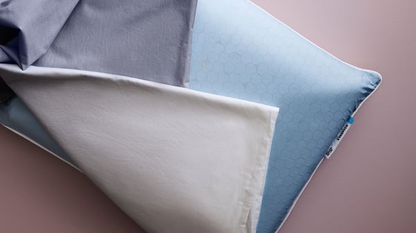 Extreme close-up of white KVARNVEN ergonomic pillow with cushioning foam on one side and cooling fabric on the other.