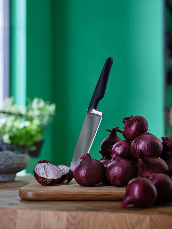 A knife is stuck upright in a wooden cutting board alongside red onions.