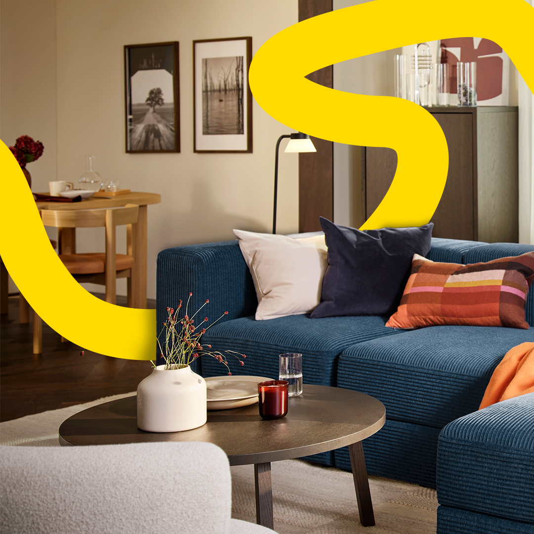 JÄTTEBO Sofa in Blau mit Kissen im Wohnzimmer und gelbem grafischem Akzent.