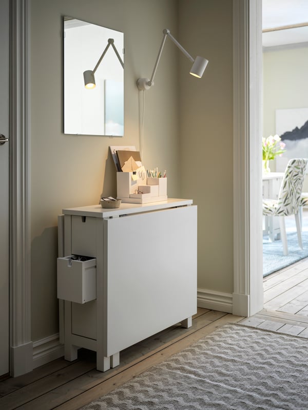 A hallway with a folded-down, white NORDEN gateleg table against a wall, and a LÄRBRO mirror a white NYMÅNE lamp above it.