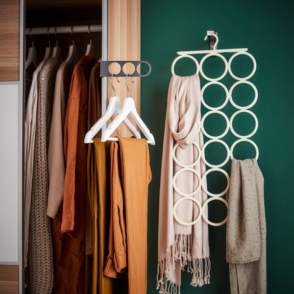 PAX wardrobe with KOMPLEMENT extendable hanger and BUMERANG hangers with clothes on them. A KOMPLEMENT multipurpose hanger is shown on a hook mounted on the wall with various scarves organised on it.