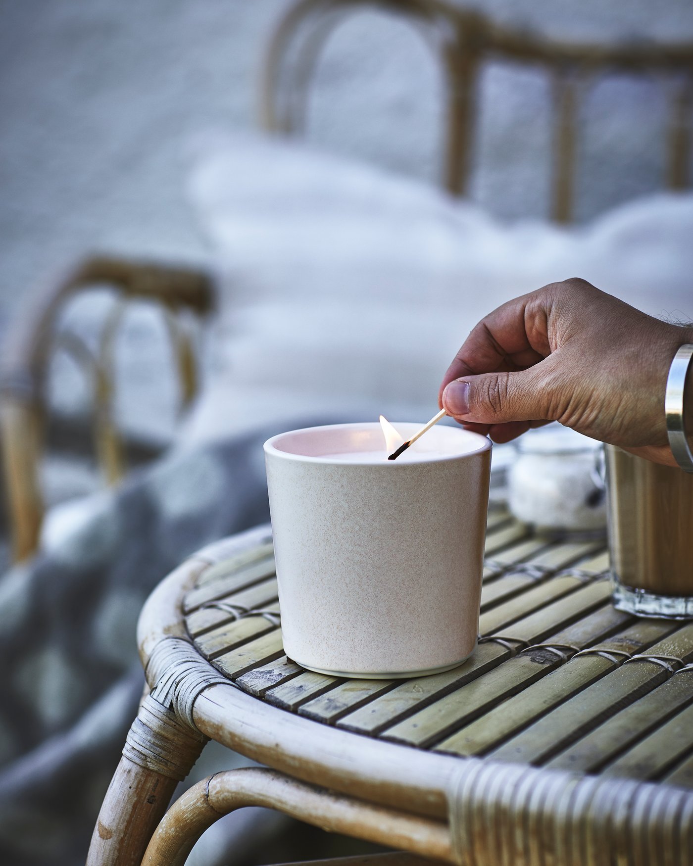 Una mano accende una candela profumata JÄMLIK alla vaniglia in un vaso di ceramica.  