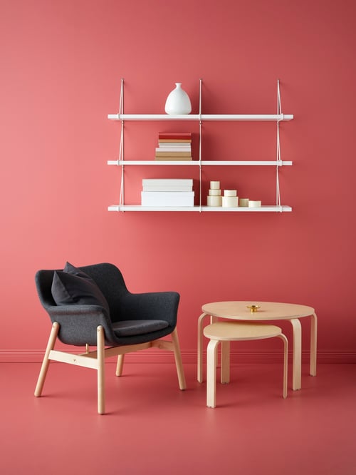 Room with red walls and floor, armchair, two tables, wall shelf combination above with books, and vase.