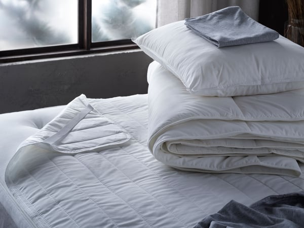 Person using hands to secure ÄNGSKORN mattress protector on top of spring mattress.