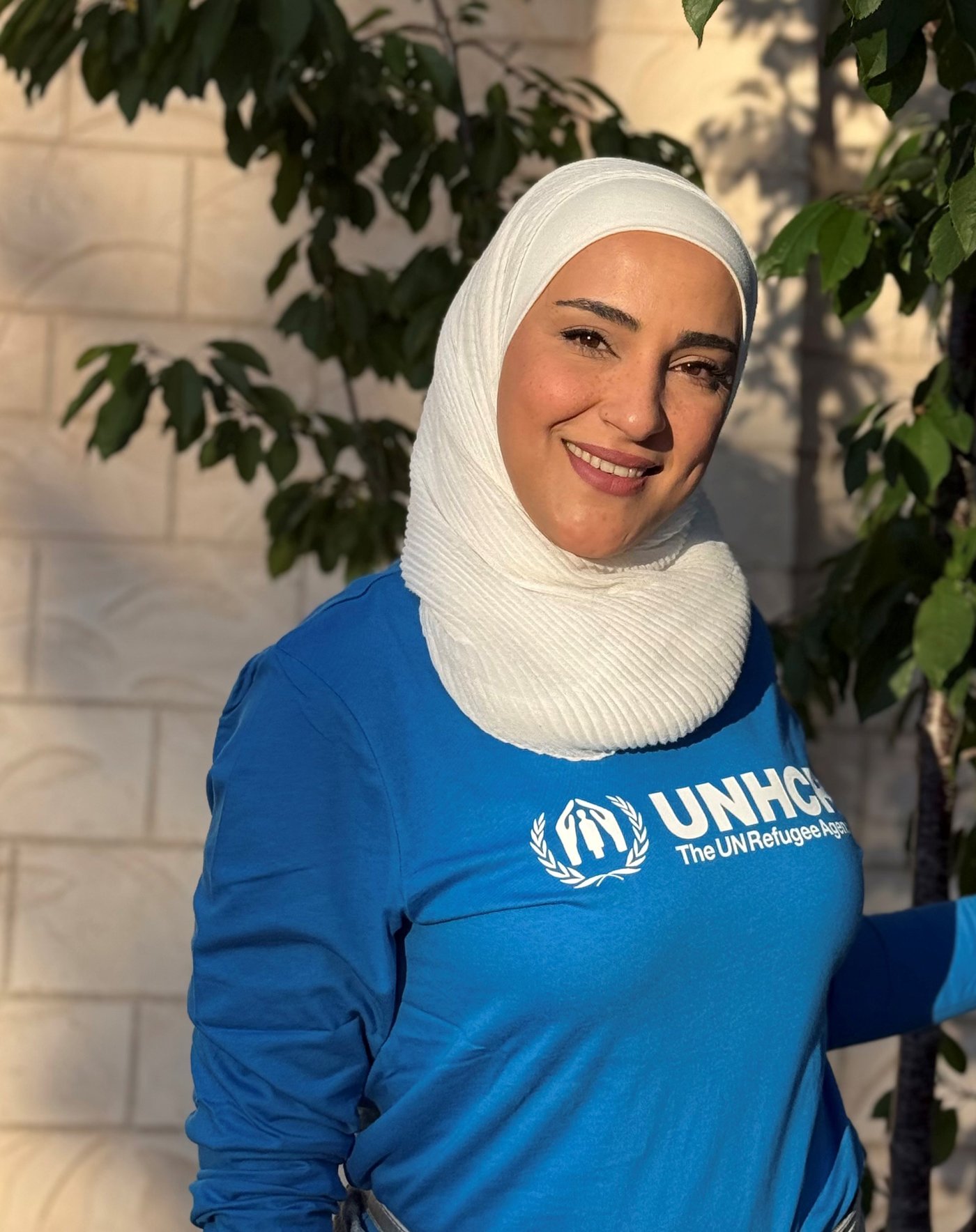 Lujain outside in the evening sun, wearing a blue UNHCR sweater.