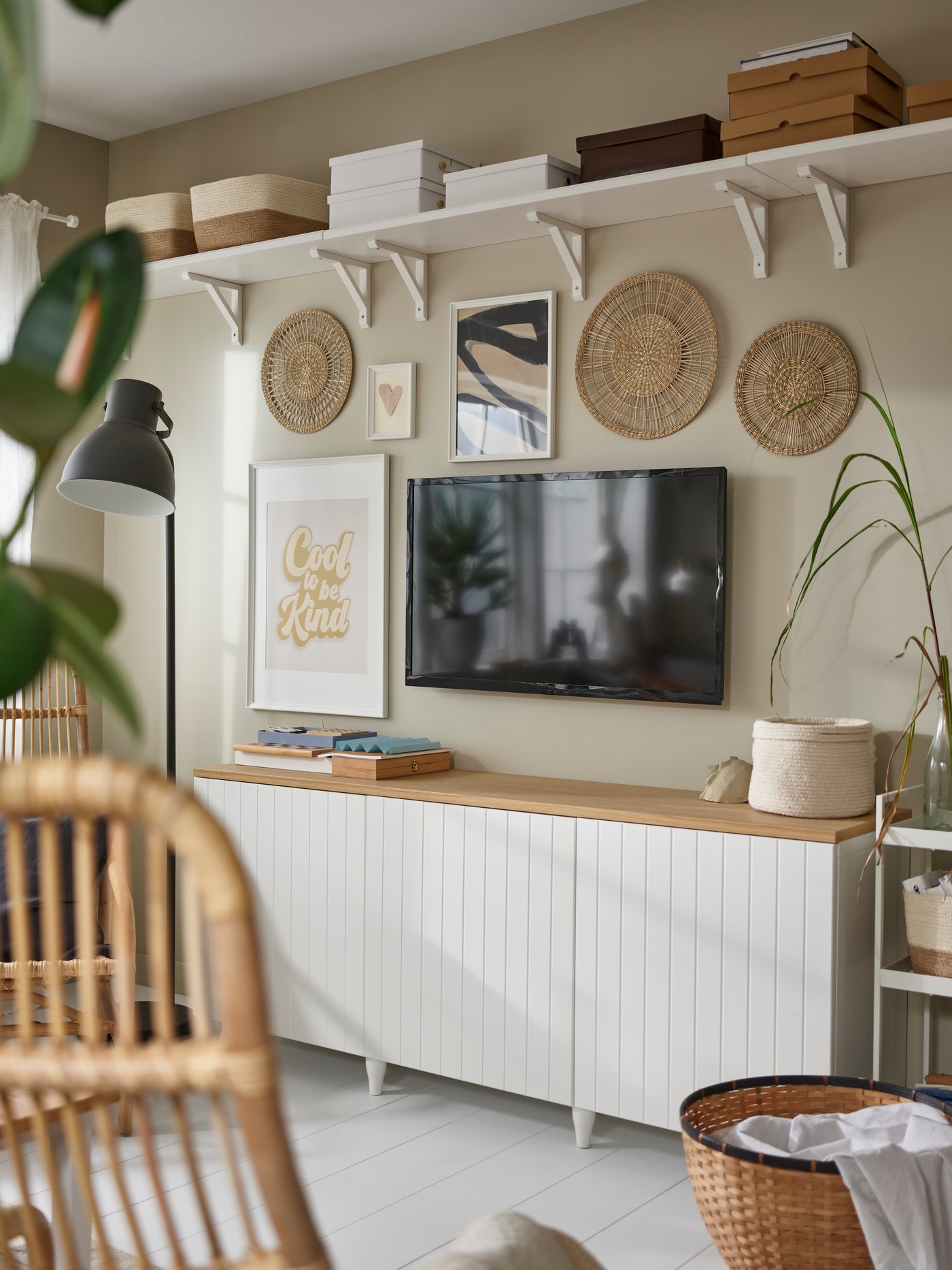 Salón con una combinación de almacenaje BESTÅ beige, colocada bajo un televisor de pared, cuadros enmarcados y adornos redondos