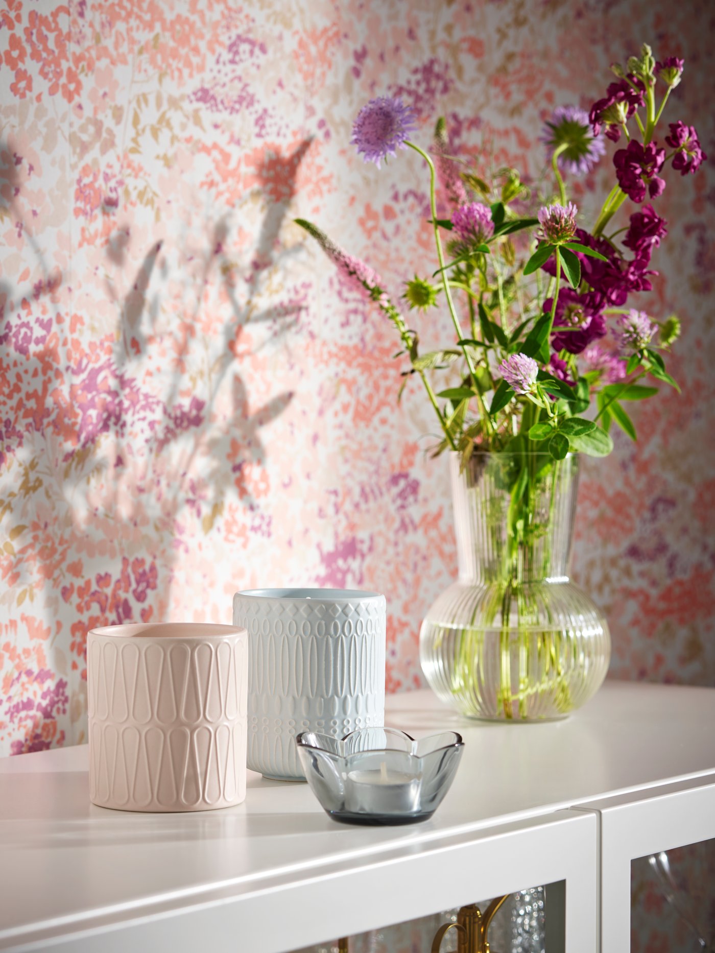 En vas med blommor står mot en rosa vägg.