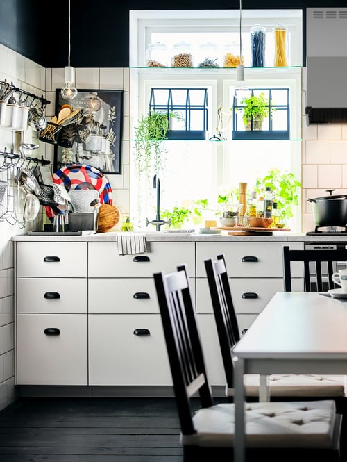 A modern kitchen that features two base cabinets with 3 drawers, a table, a brown chair, a worktop, a tray, and a pot.