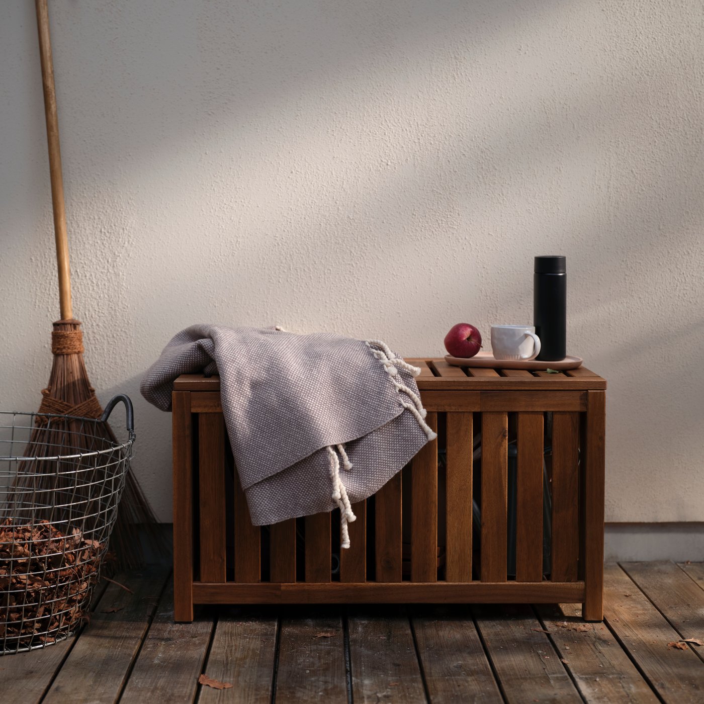 An ULLTISTEL throw and a white PANSARMAL mug sit on top of a NÄMMARÖ storage box on a terrace.