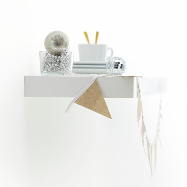 A side view of a LACK wall shelf – decorated for a party – showing where it connects to the wall without visible brackets.