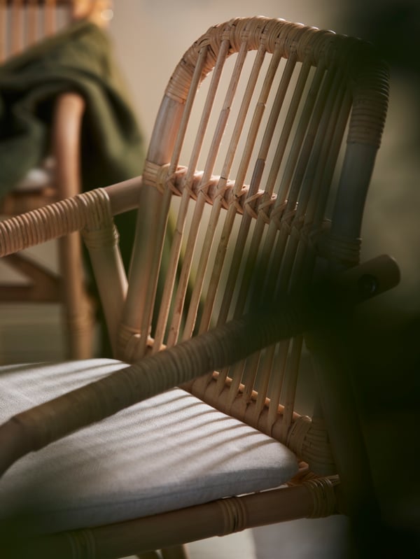 Part of a dining area with a dimly sunlit SALNÖ chair made in sturdy, braided rattan and with a GRYTTOM seat cushion.