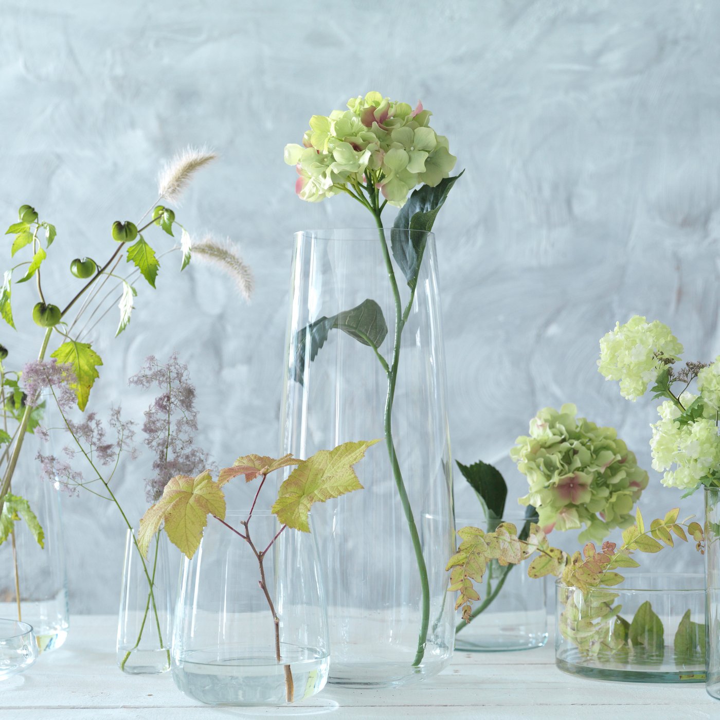 BERÄKNA vase, clear glass, and CYLINDER vases, set of 3, clear glass, on a table filled with flowers. 
