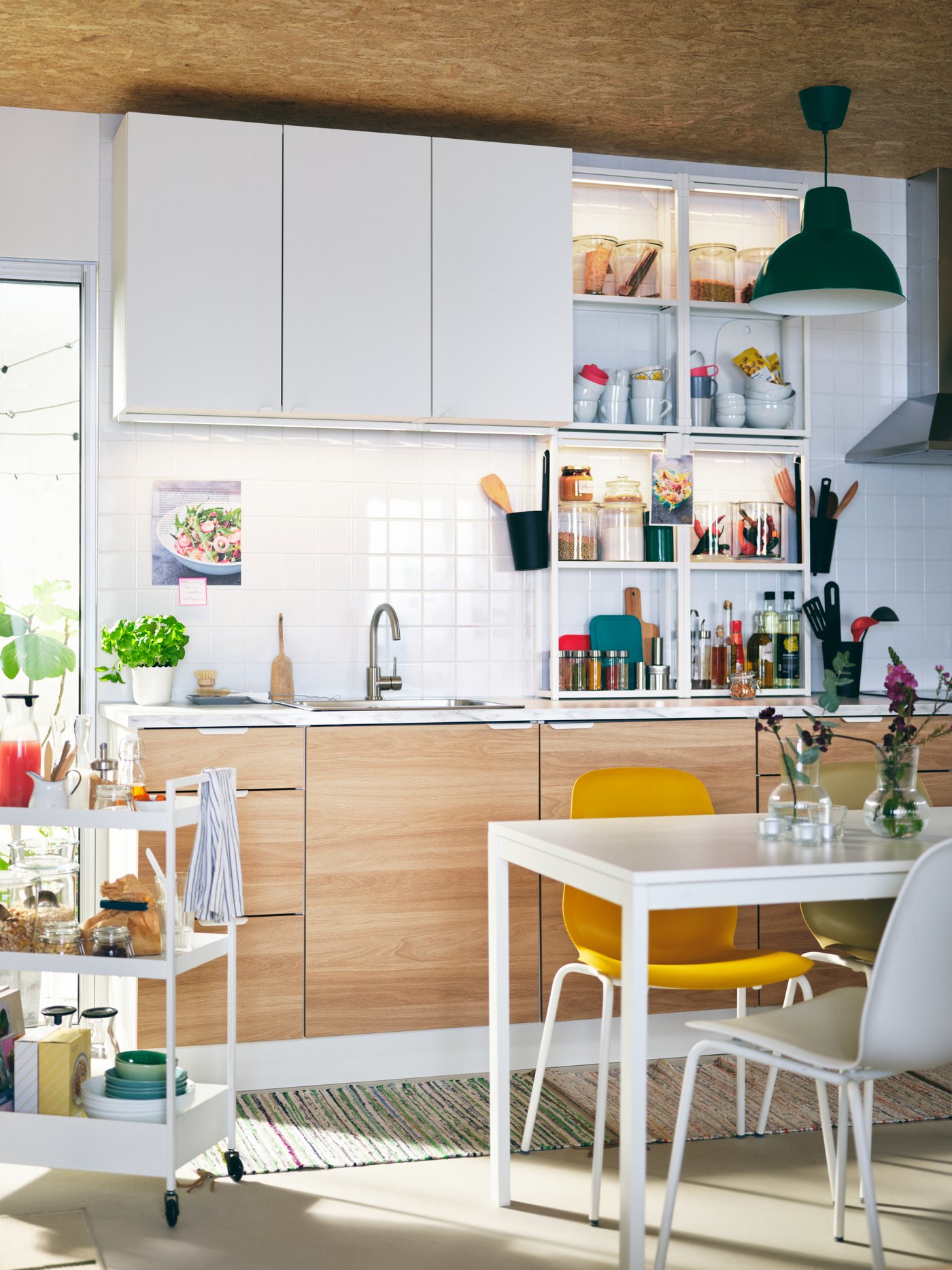 A light kitchen with ENHET cabinets, a white MELLTORP table, different-colour LEIFARNE chairs, and a white NISSAFORS trolley.