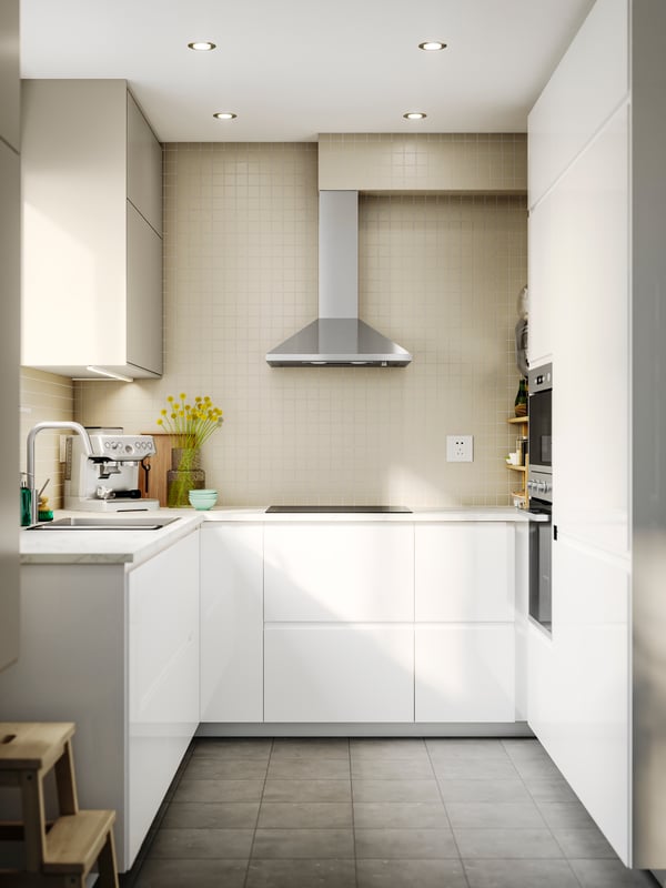A kitchen featuring VOXTORP high-gloss white fronts, a stainless steel extractor hood, and a coffee machine on the counter.