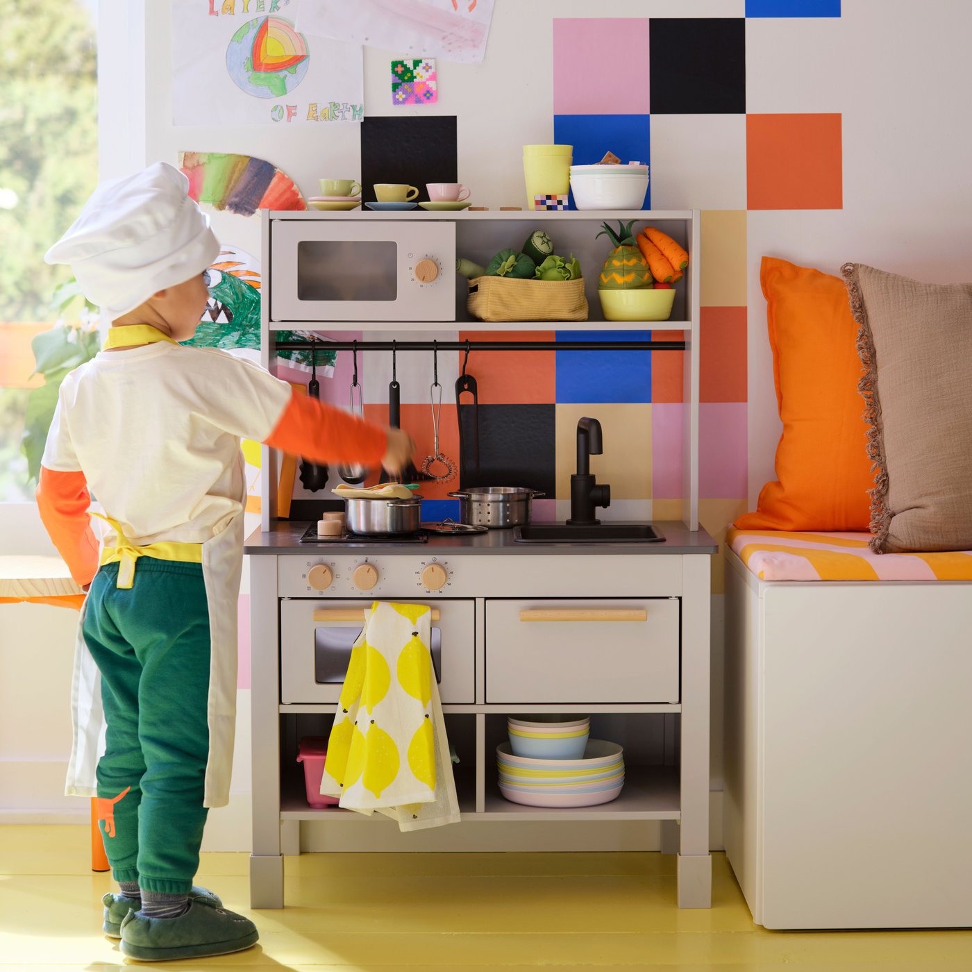 A child wearing a chef’s hat and an apron is standing by a grey SILLTRUT kitchen for children, stirring a pot on the hob. 