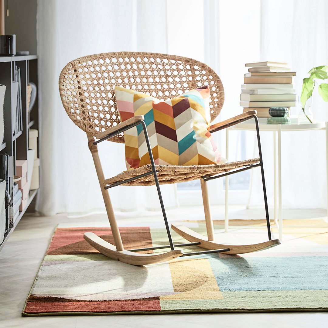 En gyngegstol med en farverig pude står på et gulvtæppe med forskellige farver.