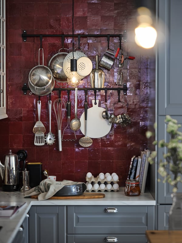 Multiple utensils hanging from black HULTARP rails in a red-tiled kitchen with a white marble-effect worktop and grey fronts.