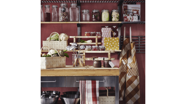 A kitchen with shelves and a table adorned with several KÖSSEBÄR items, like jars, baskets, tea towels, aprons, and more.