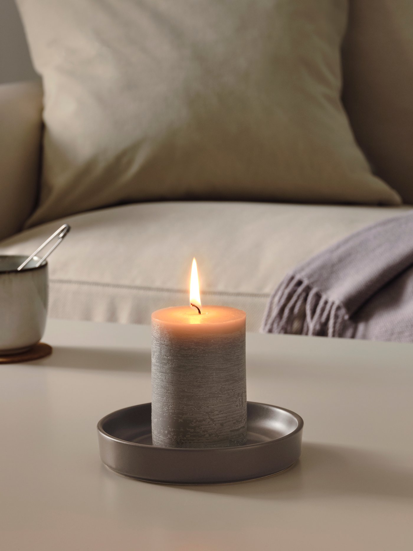 A table with a lit ADLAD scented candle in glass, next to a ÄROFULL candle dish.