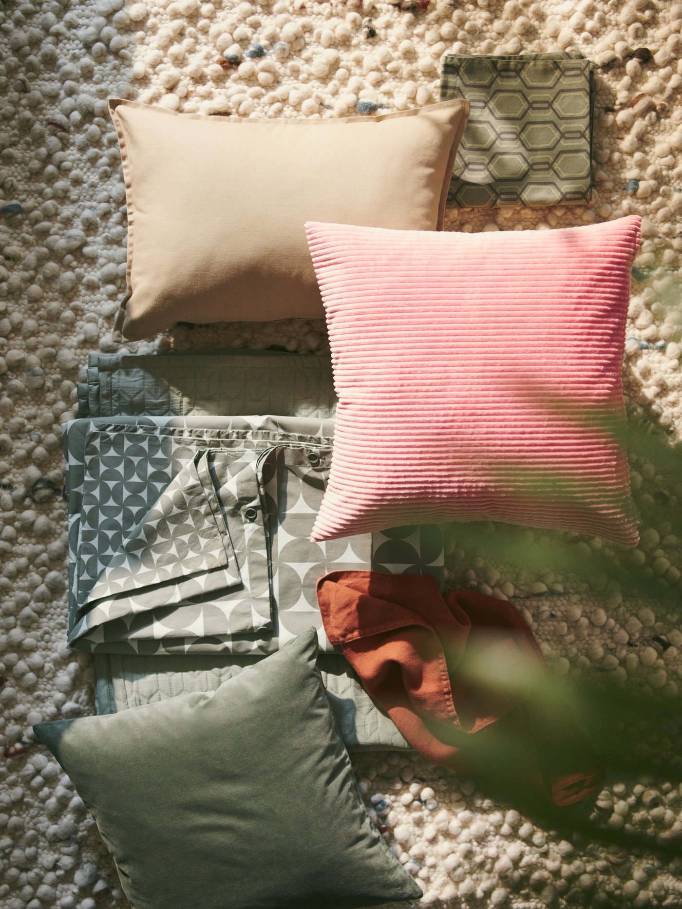 Kissen und Textilien in Beige, Salbeigrün, Rosa und Rotbraun liegen auf einem handgefertigten SVÄRDBORG Teppich.