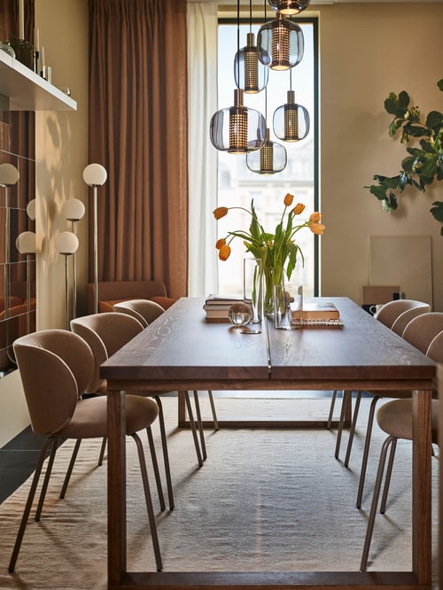 Dining area featuring a brown MÖRBYLÅNGA table, surrounded by KRYLBO chairs. A vase with flowers is on the table.