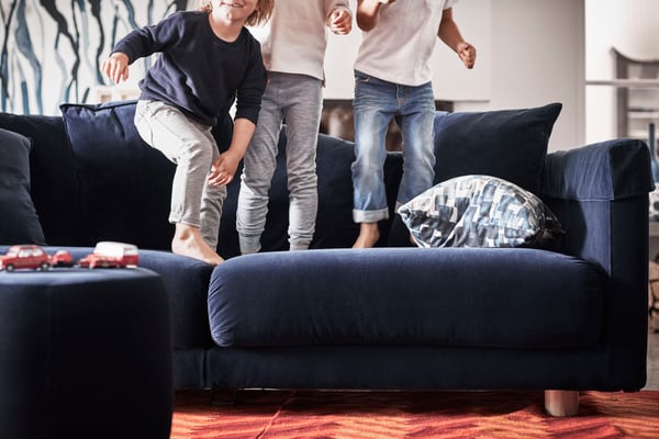 Three young children in bare feet, jumping on a dark blue sofa.
