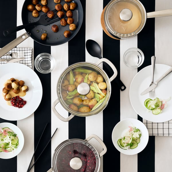 HEMKOMST cookware in stainless steel with DRAGON cutlery in stainless steel and GNARP kitchen utensils in black.