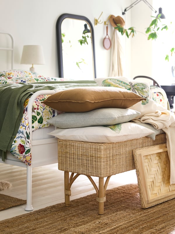 A SANDTRAV cushion piled with cushions in LAGERPOPPEL and ROTFJÄRIL covers on top of a rattan TOLKNING bench with storage.