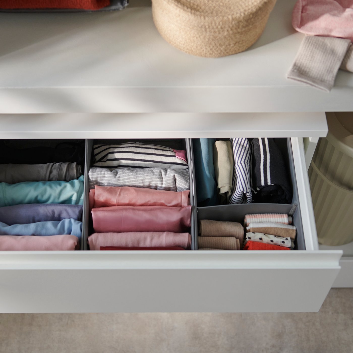 A close-up of a dark grey SKUBB box set of three, neatly organised with folded clothes in various colours.