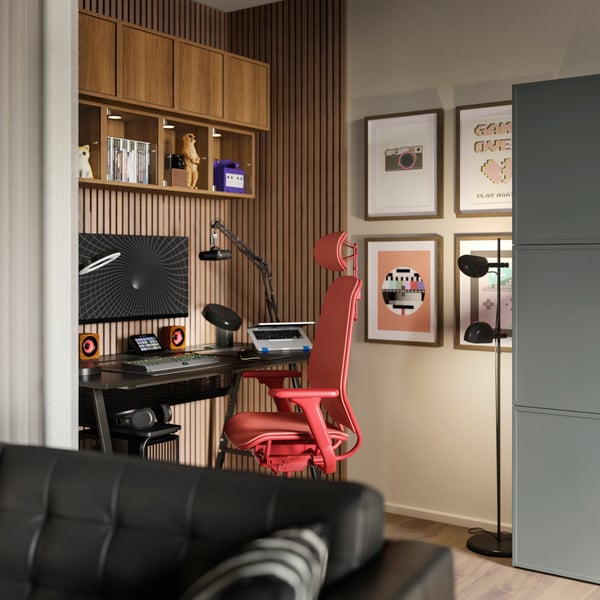 A black UTESPELARE gaming desk and a red STYRSPEL gaming chair occupy a nook of a living room. Retro prints are on the walls.