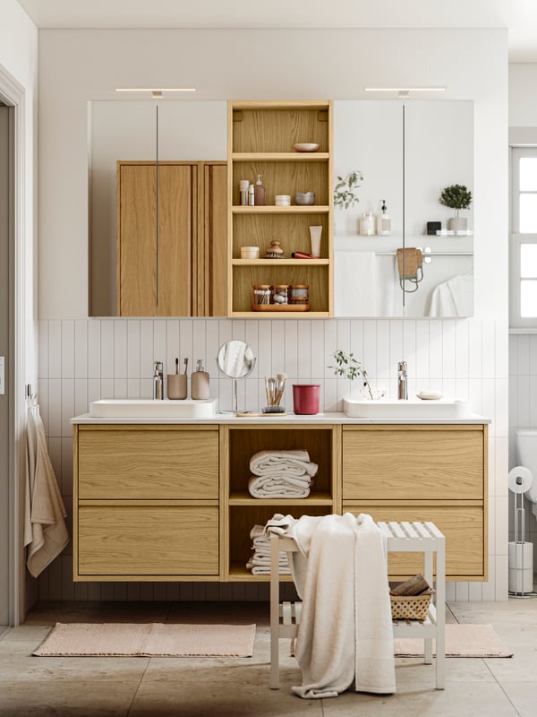 A bright bathroom has ÄNGSJÖN bathroom furniture in oak effect, including wall cabinets and a sink with drawers.