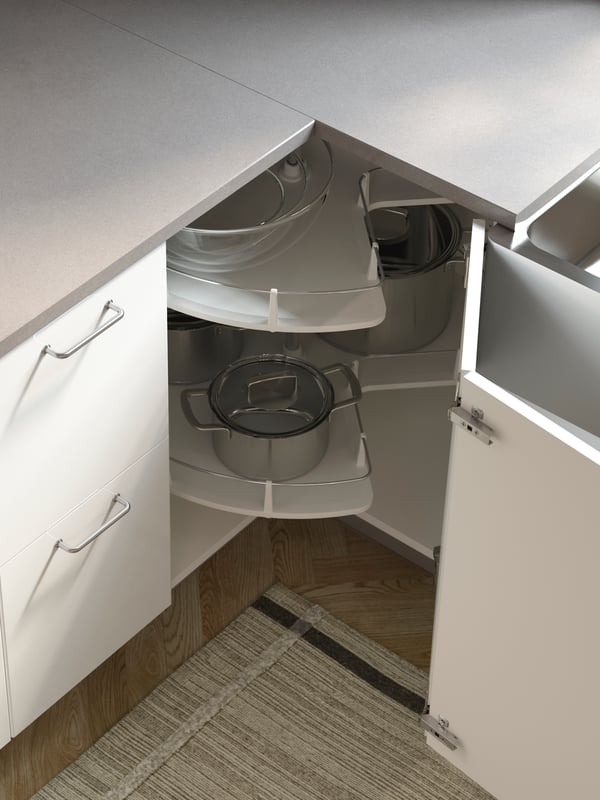 Une cuisine avec des comptoirs gris et une armoire d’angle ouverte blanche où un rangement pivotant UTRUSTA contient des casseroles, des poêles et de la vaisselle.