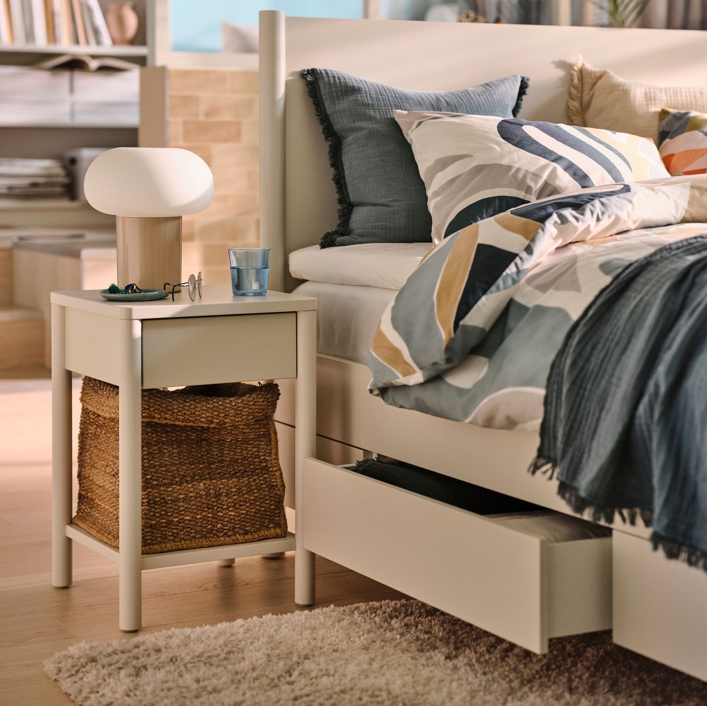 Buró TONSTAD color blanco roto junto a una cama TONSTAD color blanco roto con ropa de cama MYGGLASVINGE multicolor en un dormitorio.