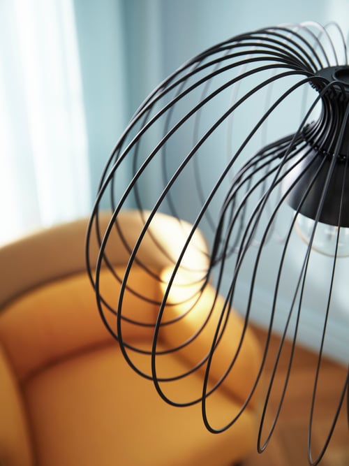 Close-up of the flowing metal lines on the KALLFRONT pendant lampshade, hanging above a yellow armchair.